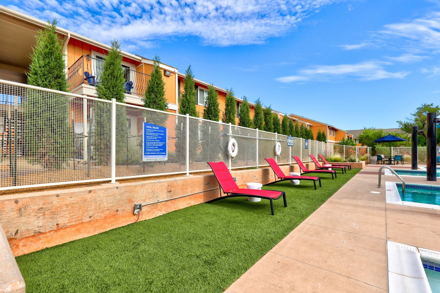 A poolside area with red chairs and a fence.